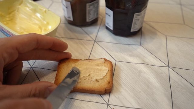 adding butter to a rusk with a knife and breaking it in two, slow motion