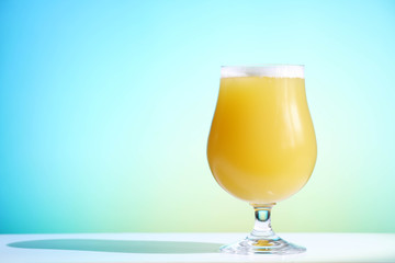 A hazy New England India pale ale beer in a tulip shaped glass against a blue background.