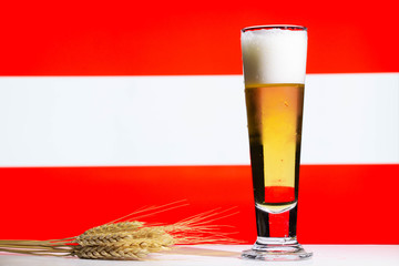 A lager style beer in a tall glass with a wheat or barley sheaf and a Austrian flag background.