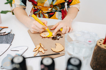 Woman hands painting handmade plywood figures on the work desk with a yellow felt-tip pen. No head.