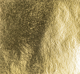 Real gold foil texture background with light reflections.