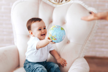 Little boy with a globe, a child learns the world through a globe at home with parents studying at home while isolated