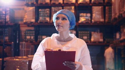 Controller checking factory storage room. Pretty young lady walking between shelves in huge storage room and making notes during inspection in factory.