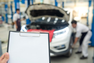 The car mechanic is closely monitoring with the writing to the clipboard of the checklist for...