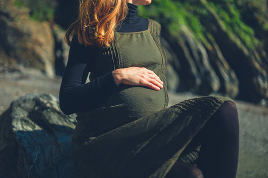 Pregnant woman sitting on rock by the sea