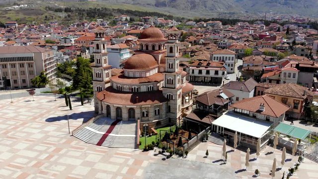 Peaceful city square in Korca, Albania with Orthodox Cathedral and traditional houses with red roofs and mountain background