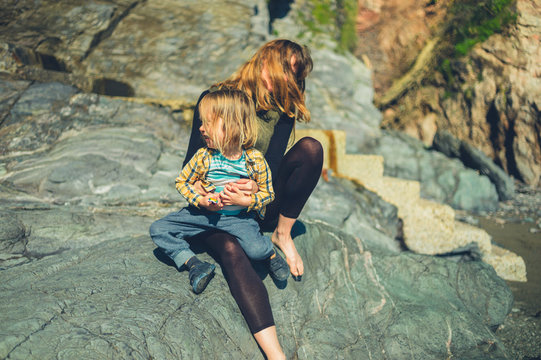 Preschooler sitting in mother's lap on a rock by the coast