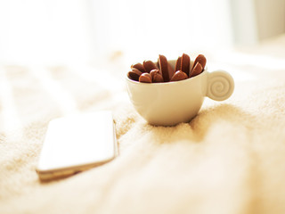 A cup of coffee or tea with chocolate biscuits  standing on the bed early in the morning with a mobile phone next to it