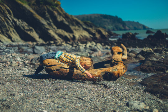 Preschooler lying on driftwood and playing with toy car