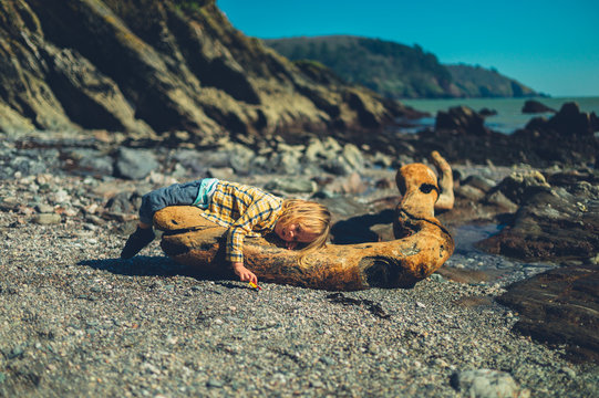 Preschooler lying on driftwood and playing with toy car