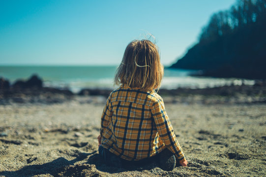 Little preschooler sitting on the beach in springtime