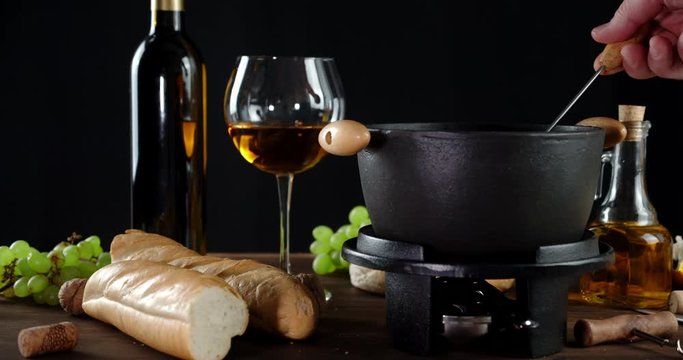 The man's hand dunks a piece of bread in fondue with wine.