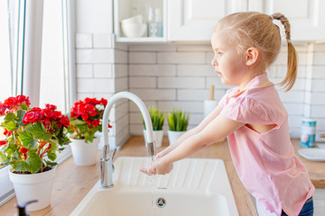 Blonde toddler girl washing hands in the lingh kitchen before eating. Hygiene and healthcare concept.