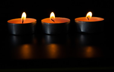 Composition of three candles on dark luxury night background. Black table, side view. Candles Burning at Night. Orange taper burning in focus, foreground. illustration design.