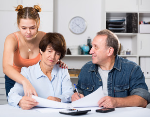 Smiling parents are reading utility bill with their adult daughter