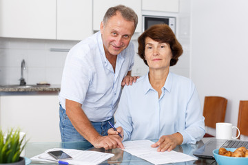 Mature family couple sitting at kitchen  and woman signing documents