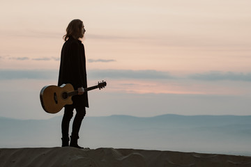 long haired bearded guy with guitar standing in the sunset