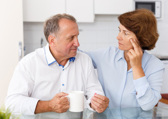 Mature family couple sitting at kitchen table and taking medicine indoors