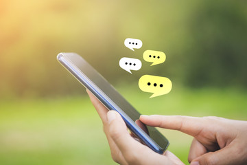 Close up woman hand hold using smart phone with chat icon flying at outdoor nature park background....