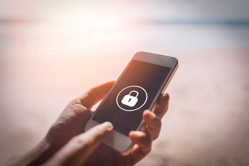 Woman hand using smartphone at sunset beach with lock icon background. Technology business and...