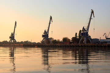 Port cranes, harbour cranes on the river bank at sunset