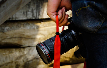 A photographer holds a camera with a red strap.