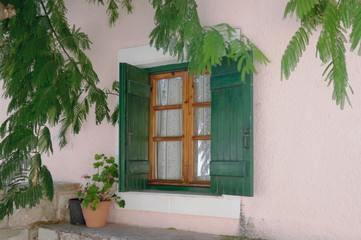 A window with green wooden shutters against a pink stucco wall