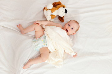 baby in diaper lies on her back on the bed