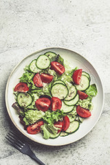 Fresh tomato and cucumber salad in white bowl, gray background. Healthy food concept.