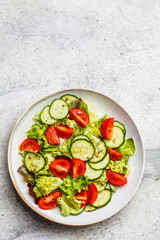 Fresh tomato and cucumber salad in white bowl, gray background. Healthy food concept.