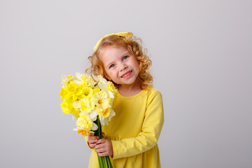 little  curly haired girl in a yellow dress holding a bouquet of spring flowers on a white background smiles