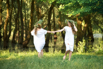 Naklejka na ściany i meble Two girls with wreaths of flowers in their hands. Midsummer. Earth Day.