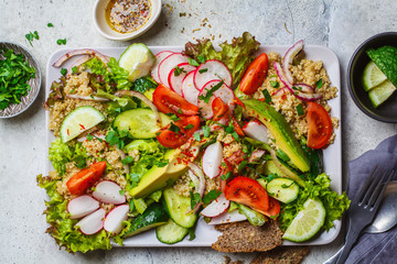 Quinoa salad with tomato, cucumber, radish and avocado on gray plate, top view. Healthy vegan food concept.