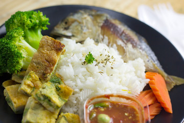 Mackerel with steamed rice in a black plate decoration with broccoli vegetables and carrots.