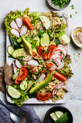 Quinoa salad with tomato, cucumber, radish and avocado on gray plate, top view. Healthy vegan food concept.