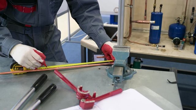 The worker measures and bends a thin copper tube.
