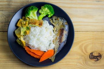 Mackerel with steamed rice in a black plate decoration with broccoli vegetables and carrots.