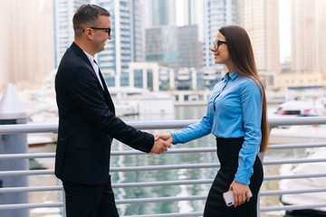 Business man and woman standing in the city and shaking their hands on skyscrapers background