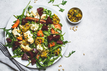 Baked sweet potato, cauliflower and beetroot salad with mustard dressing in white plate, top view....