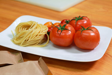 Raw pasta noodles with fresh tomatoes on a white plate. Fresh spaghetti ingredients on the wooden table.