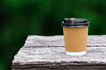 Disposable coffee paper cup mockup on stone table with nature green blurred background