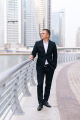 Handsome young business man standing agains skyscrapers outdoors