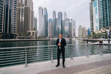 Fototapeta na wymiar Successful young businessman wearing suit and sunglasses walking on street in business district