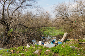 Heap of household trash lying among green grasses in a nature landscape