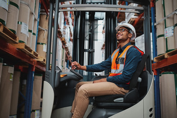 African forklift driver focused on carefully transporting stock from shelves of a large warehouse...