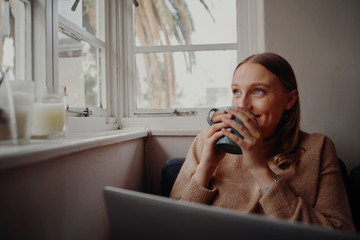 Self isolated young woman smiling enjoying work from home drinking coffee and daydreaming