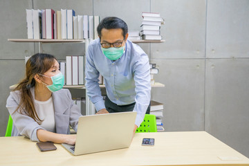 Asian female and Businessman workers meeting together with laptop and wear protective masks prevent PM 2.5 and corona viruus or covic19 at co working space .Health and teamwork concet