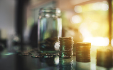 Coins stack and a glass money jar on the table for saving and financial concept