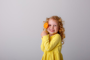 little curly blonde girl smiling holding a Lollipop hiding on a white background
