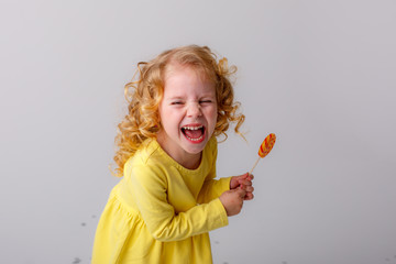 little curly blonde girl smiling holding a Lollipop hiding on a white background